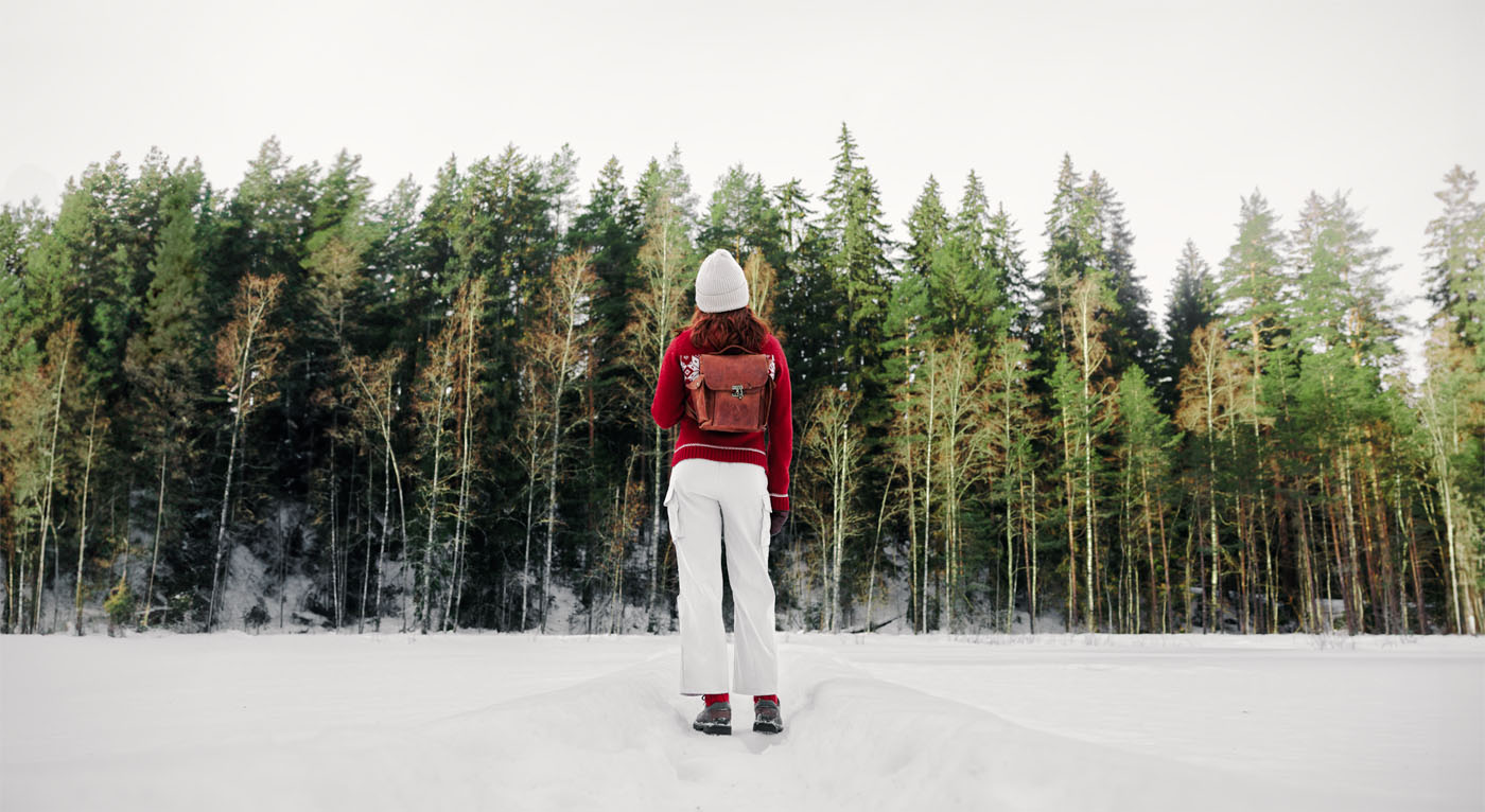 Jossain pohjoisessa -esityksen julistekuvassa teatteriopiskelija punainen villapaita päällä seisoo selkä kameraa kohti lumisella alueella metsän ollessa taustalla